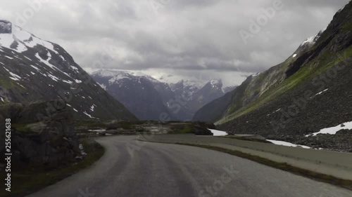 Driving down Gamle Strynefjellsvegen Riksvei 258 the old mountain road in Strynefjell, Oppland in the Norwegian mountains with snow and ice covered mountains in the background at a cloudy day. photo