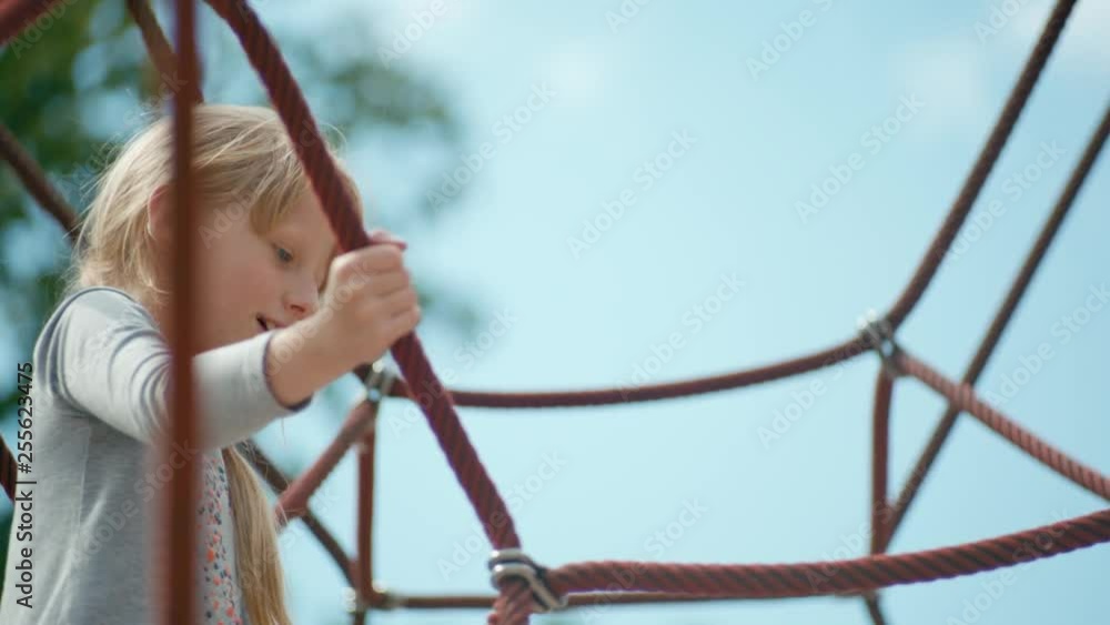 Low Angle Shot of a 7 year old Blond Girl in a Dress Playing High on Net Climber on the Playground in Summer Low Angle Shot of a 7 year old Blond Girl in a Dress Playing High on Net Climber on the Playground in Summer