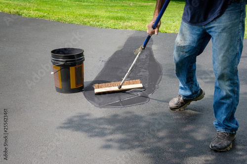 Obraz na plátne Homeowner spreads blacktop asphalt sealant on driveway