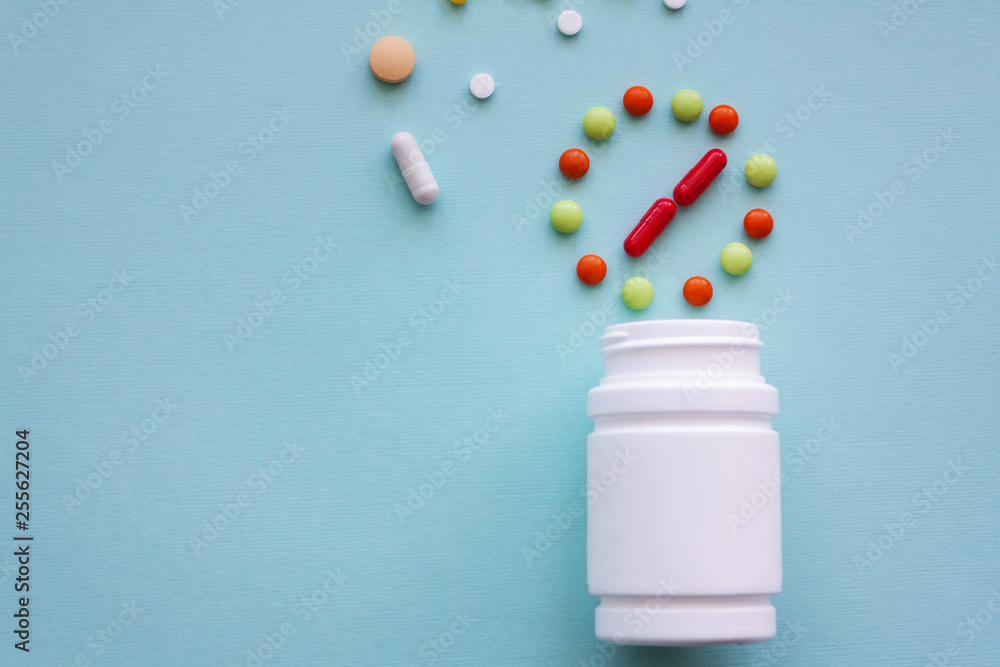 Multicolored pills from white jars on a blue background Multicolored pills from white jars on a blue background