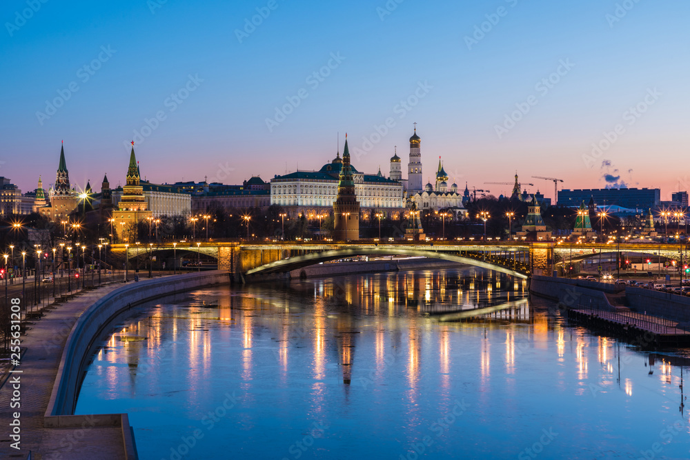 Illuminated Moscow Kremlin and Bolshoy Kamenny Bridge in the rays of rising sun. View from the Patriarshy pedestrian Bridge in Russia. Morning urban landscape in the blue hour