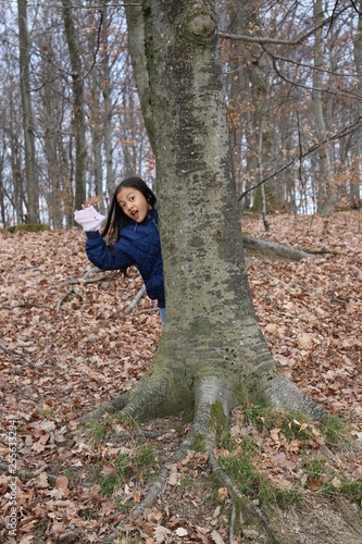Jeune fille enfant asiatique cachée derrière un arbre faisant coucou d'une main