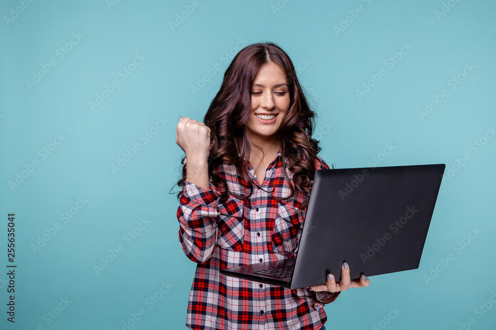 Portrait of an excited young girl holding laptop computer and celebrating success isolated over blue background Portrait of an excited young girl holding laptop computer and celebrating success isolated over blue background