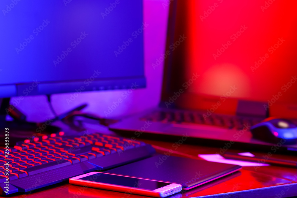 Workplace digital designer. Freelancer workplace in neon light. Computer, graphics tablet and smartphone on the table. Place for creativity in blue pink light Workplace digital designer. Freelancer workplace in neon light. Computer, graphics tablet and smartphone on the table. Place for creativity in blue pink light