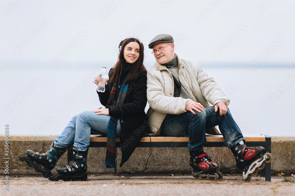 A young girl on roller skates and her father of retirement age are sitting on a bench and smiling at each other. Water and sport. The concept of thirst.