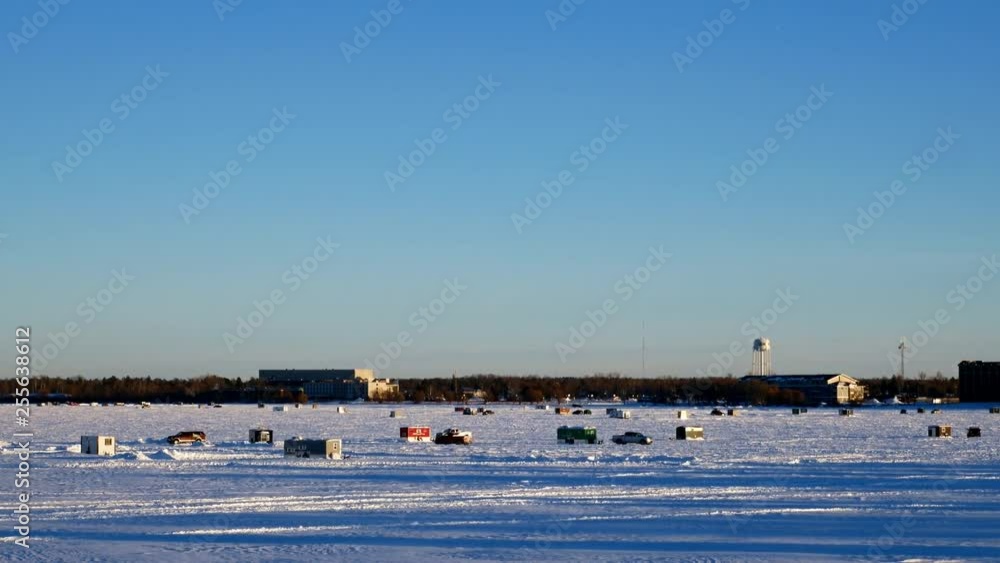 Car drives past Winter Fishing Houses on frozen Lake Bemidji in Minnesota on a late December afternoon in the city of Bemidji, Minnesota with slow zoom in. Car drives past Winter Fishing Houses on frozen Lake Bemidji in Minnesota on a late December afternoon in the city of Bemidji, Minnesota with slow zoom in.