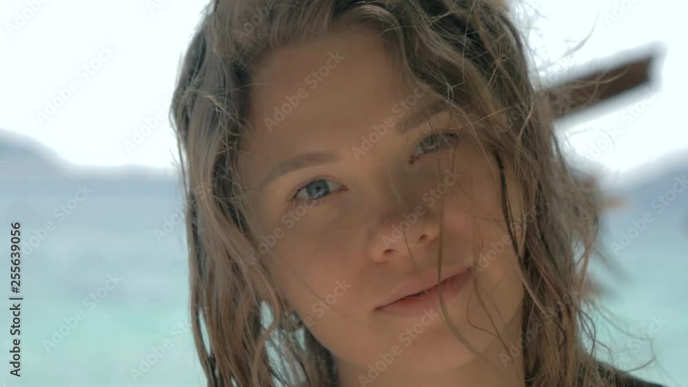 Close-up portrait of beautiful european young woman looking in the camera, hair blowing in wind on tropical beach, blue sea on the background. Travel concept. Close-up portrait of beautiful european young woman looking in the camera, hair blowing in wind on tropical beach, blue sea on the background. Travel concept.