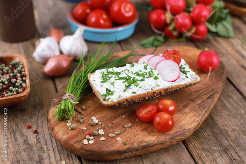 healthy breakfast -  wholemeal roll with quark and fresh chives, radishes and tomato on a rustic wooden table - healthy breakfast