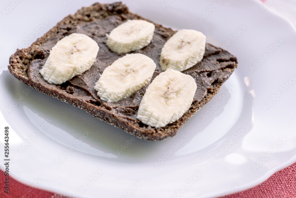 Healthy rye bread with carob and banana on the white plate. Healthy concept.