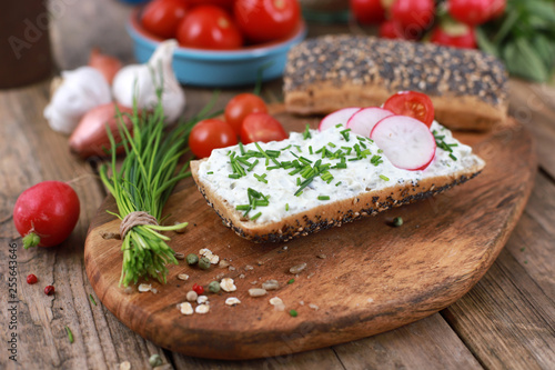 healthy breakfast - wholemeal roll with quark and fresh chives, radishes and tomato on a rustic wooden table - healthy breakfast