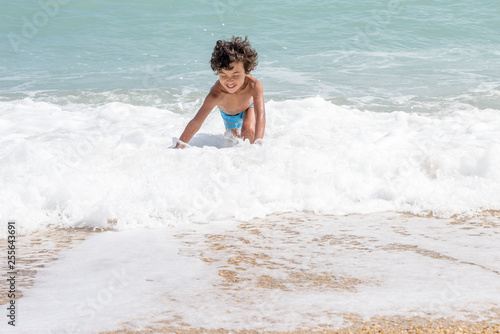 Happy kid playing on the beach in rough waters during a summer vacation