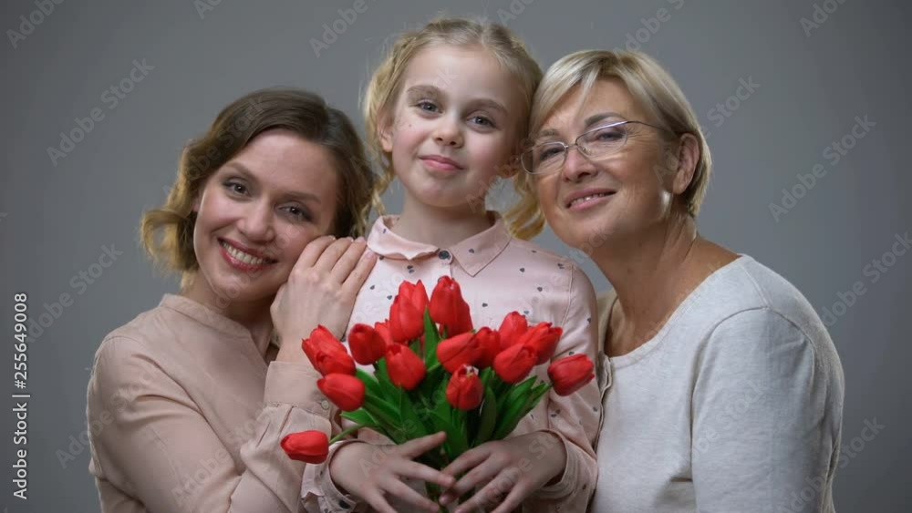 Beautiful granny and mother hugging daughter with tulips in hands, generations Beautiful granny and mother hugging daughter with tulips in hands, generations