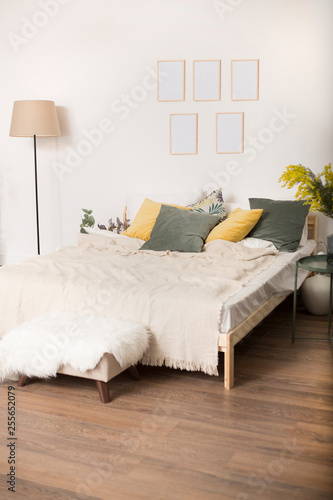 room with a bed, yellow and green pillows, a light padded stool, a floor lamp and a framework on a wall