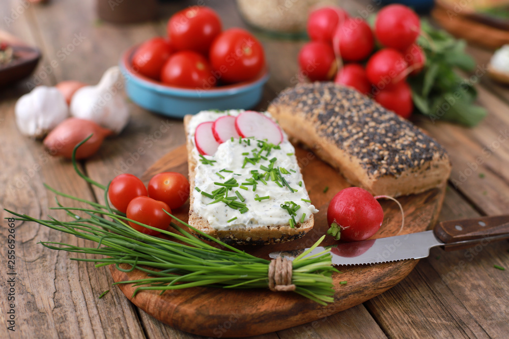 wholemeal roll with quark and fresh chives, radish and tomatoes on a rustic wooden table - healthy breakfast with fresh herbs - close up wholemeal roll with quark and fresh chives, radish and tomatoes on a rustic wooden table - healthy breakfast with fresh herbs - close up