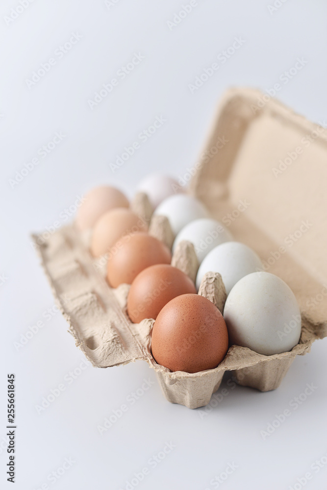Chicken eggs and duck eggs are arranged in a gradient color tone in eco carton on white background.(perspective view)