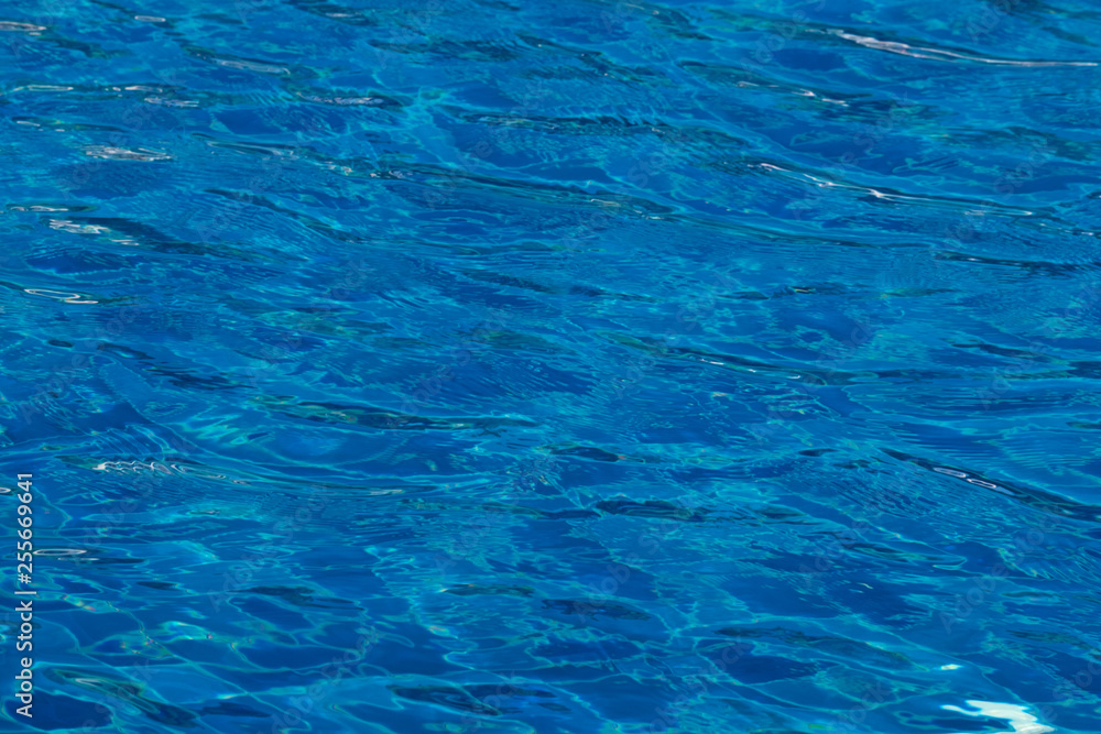 Blue and bright ripple water surface in swimming pool with sun reflection.