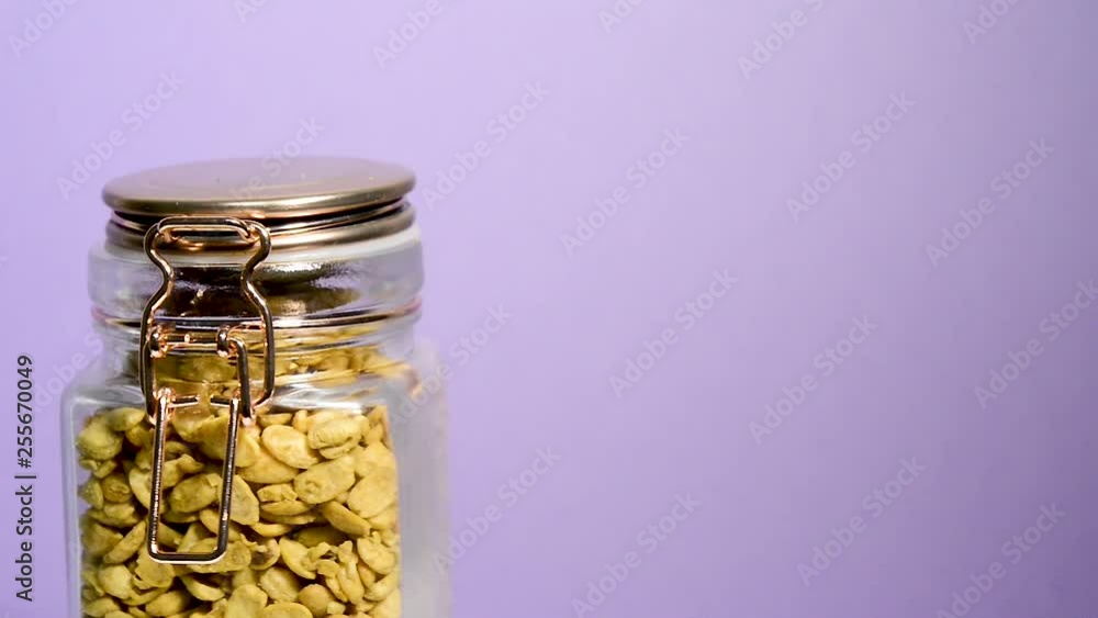 Close up of an airtight mason jar rotating with dry toasted soybeans halves on a neon lilac background. Flat plane. Eye level Close up of an airtight mason jar rotating with dry toasted soybeans halves on a neon lilac background. Flat plane. Eye level