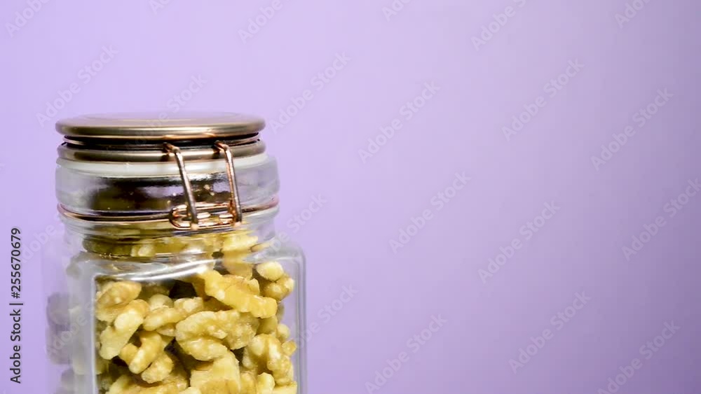Close up of an airtight mason jar rotating with shelled walnuts pieces on a neon lilac background. Flat plane. Eye level Close up of an airtight mason jar rotating with shelled walnuts pieces on a neon lilac background. Flat plane. Eye level