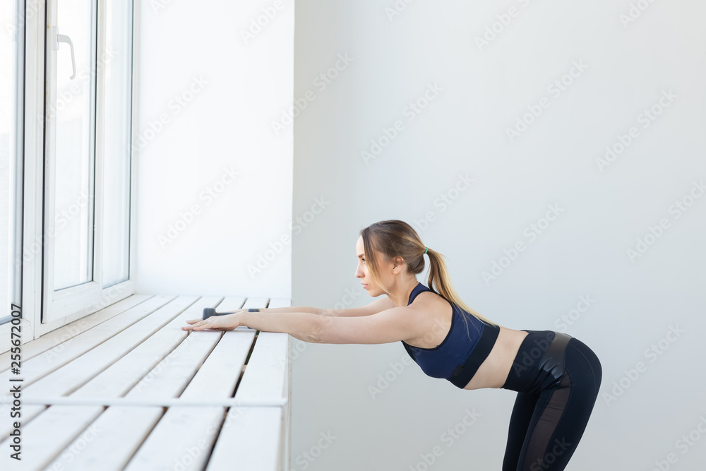 People, sport and fitness concept - young woman doing exercises stretching near window People, sport and fitness concept - young woman doing exercises stretching near window