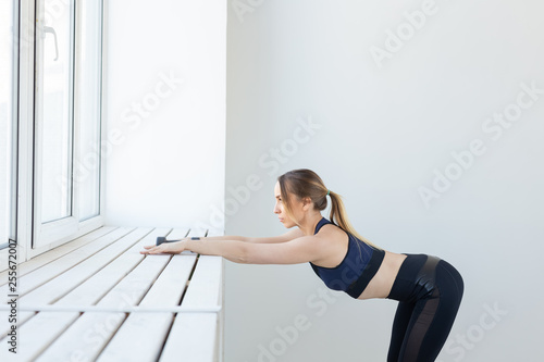 People, sport and fitness concept - young woman doing exercises stretching near window