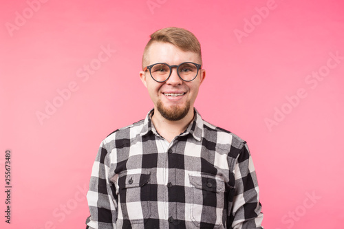 Portrait of a smiling bearded man in eyeglasses looking at camera isolated over pink background