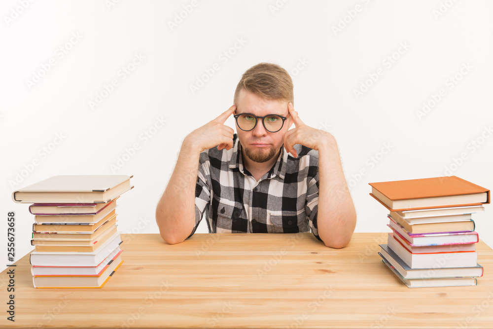 People, knowledge and education concept - Tired male student sitting at the table with mountains of books and does not want to study up People, knowledge and education concept - Tired male student sitting at the table with mountains of books and does not want to study up
