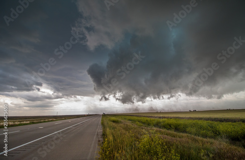 Severe winds from a dark storm cloud blow dirt across a highway on the plains.