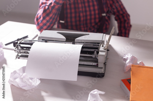 Writer's day and technology concept - Handsome writer surrounded by scraps of paper focused on work over grey background