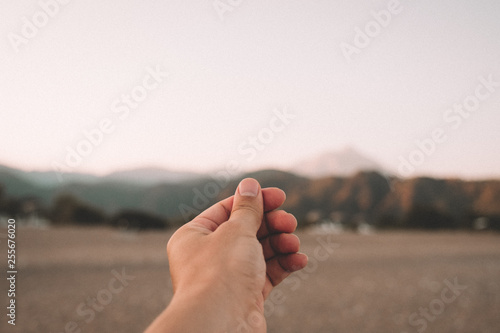 A hand simulates holding a photo, postcard or note on beautiful sunset over the mountains at the beach in summer day.
