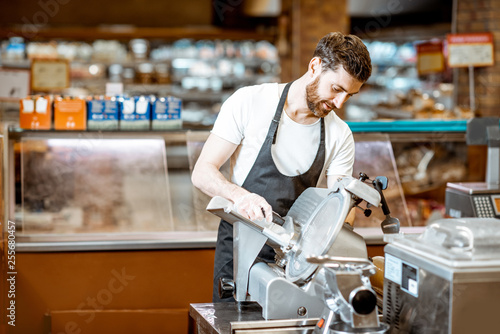 Handsome worker in uniform slicing cheese with cutting machine in the supermarket © rh2010