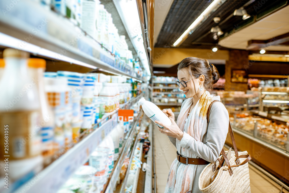 Young woman choosing milk standing near the shelves with dairy products in the supermarket
