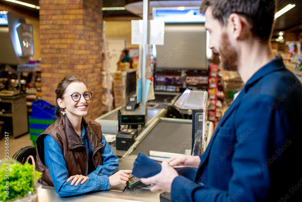 Obraz premium Businessman with happy woman cashier at the cash register buying food in the supermarket
