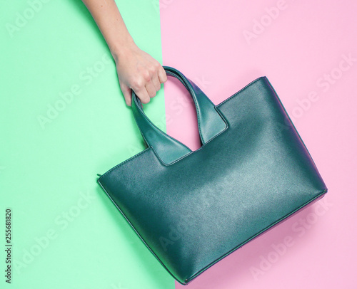 Female hand holds leather handbag on pastel background. Top view. Flat lay style, minimalism.