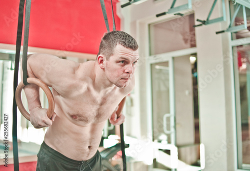 Fototapeta Naklejka Na Ścianę i Meble -  Muscular man with naked torso doing exercise on gymnastic rings at gym