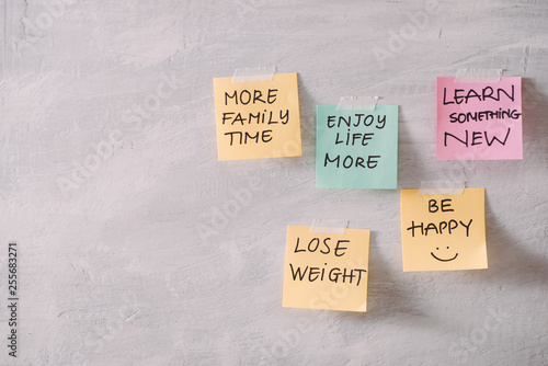 Group of New year Resolution Notes on pink, yellow, orange and green on wall written with message of more family time, lose weight and be happy