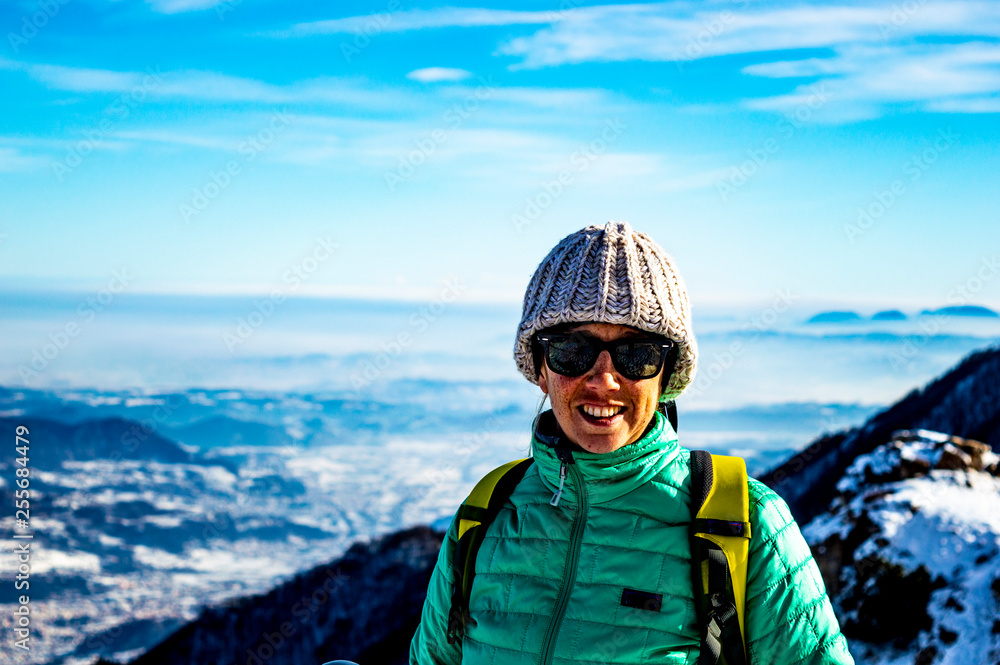 portrait of a woman on the alps wearing technical mountain clothing and the Italian plain in the background, with snow and a winter sky