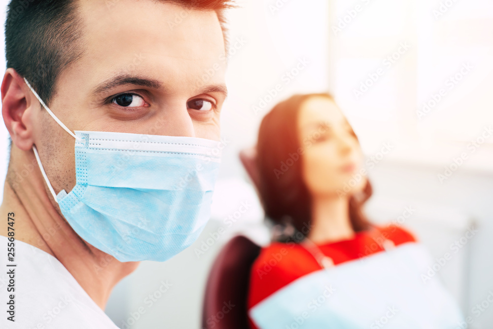 Consult a dentist. Hazel deep eyes of the dentist with short brown hair in ear loop face mask and medical uniform in front of the his new patient. Consult a dentist. Hazel deep eyes of the dentist with short brown hair in ear loop face mask and medical uniform in front of the his new patient.