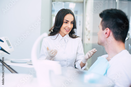 Dental clinic. Professional dentist in spacious dentist room  is wearing medical clothes and giving some recommendations to her patient after his appointment.
