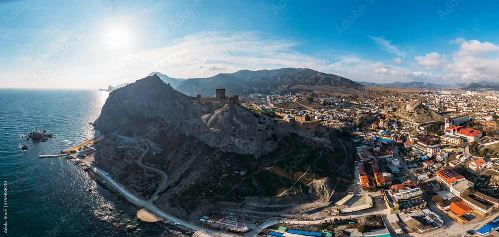 Obraz premium Genoese fortress in Sudak, Crimea. Aerial panorama view of ruins of ancient historic castle on crest of mountain near sea and small town at foot of rocks. Beautiful summer tourist landscape