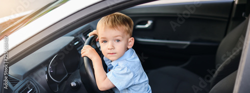 Banner. A blond boy with blue eyes sits in the front seat behind the wheel of a white car.