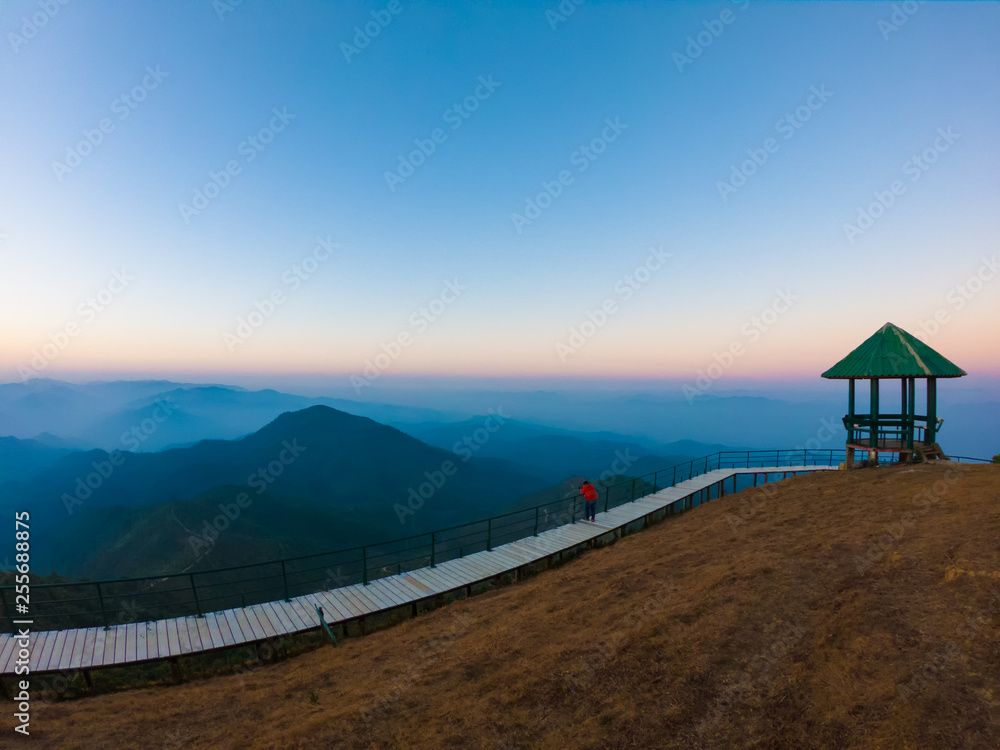 Lonely pavilion against a blue sky during morning sunrise on mountain peak with single male tourist standing on beautiful corridor along the cliff.Autumn landscape with a lonely pavilion.