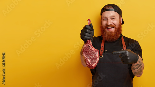 Φωτογραφία Indoor shot of man works at meat packing plant, points at ribeye steak, involved