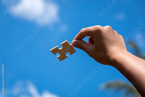 Pieces of jigsaw puzzle in woman's hands with blue sky background