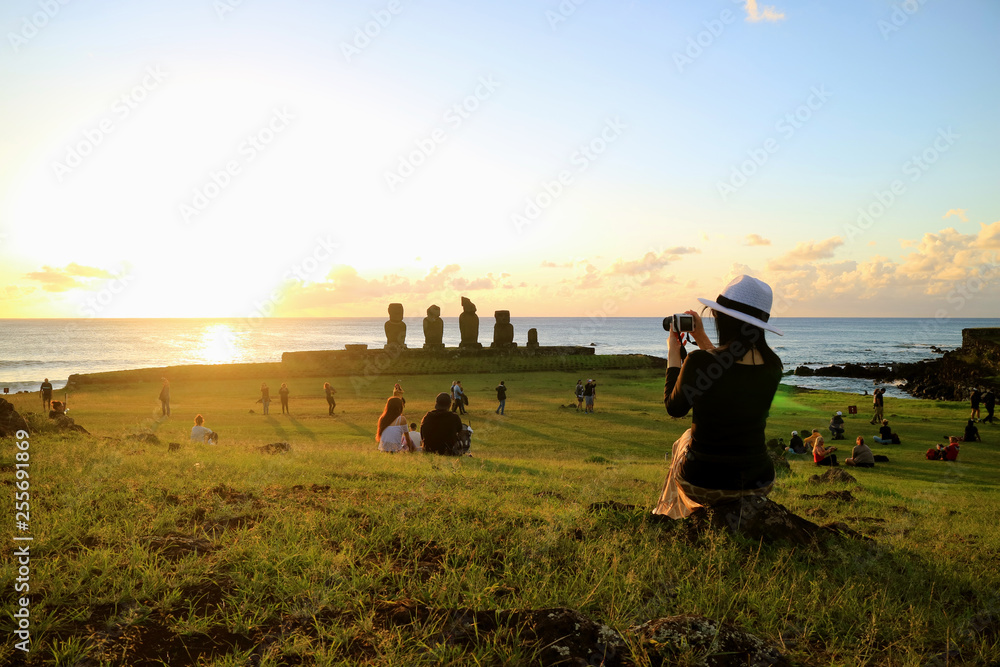 Female Tourist Taking Photos of the Famous Sunset Scene at Ahu Tahai, Easter Island, Chile  - obrazy, fototapety, plakaty 