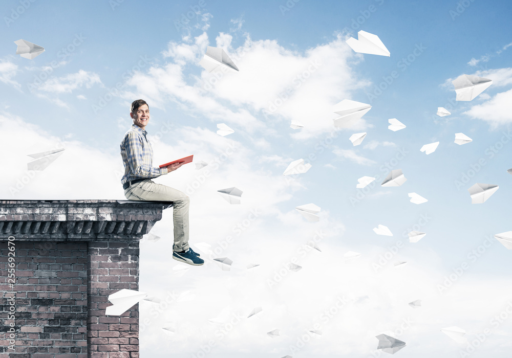 Handsome student guy on roof edge reading book and paper planes Handsome student guy on roof edge reading book and paper planes