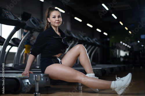 Fitness girl posing in the gym sitting on the treadmill, showing off their egs