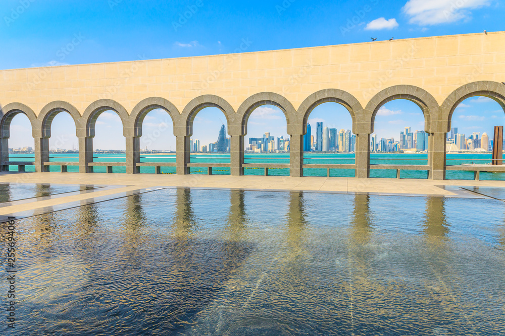Modern skyscrapers of Doha West Bay skyline through series of arches along a walkway from museum in Qatari capital. Doha in Qatar seafront. Middle East, Arabian Peninsula in Persian Gulf.