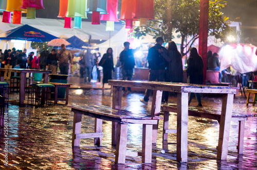Rainy evening in delhi at food festival with wet reflections on ground and food kiosks and people in the background