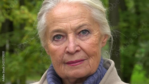 An elderly woman looks seriously at the camera in a park - face closeup