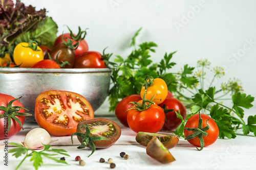 Food vegetables tomatoes of different varieties in a bowl and on a white wooden table. Rustic still life